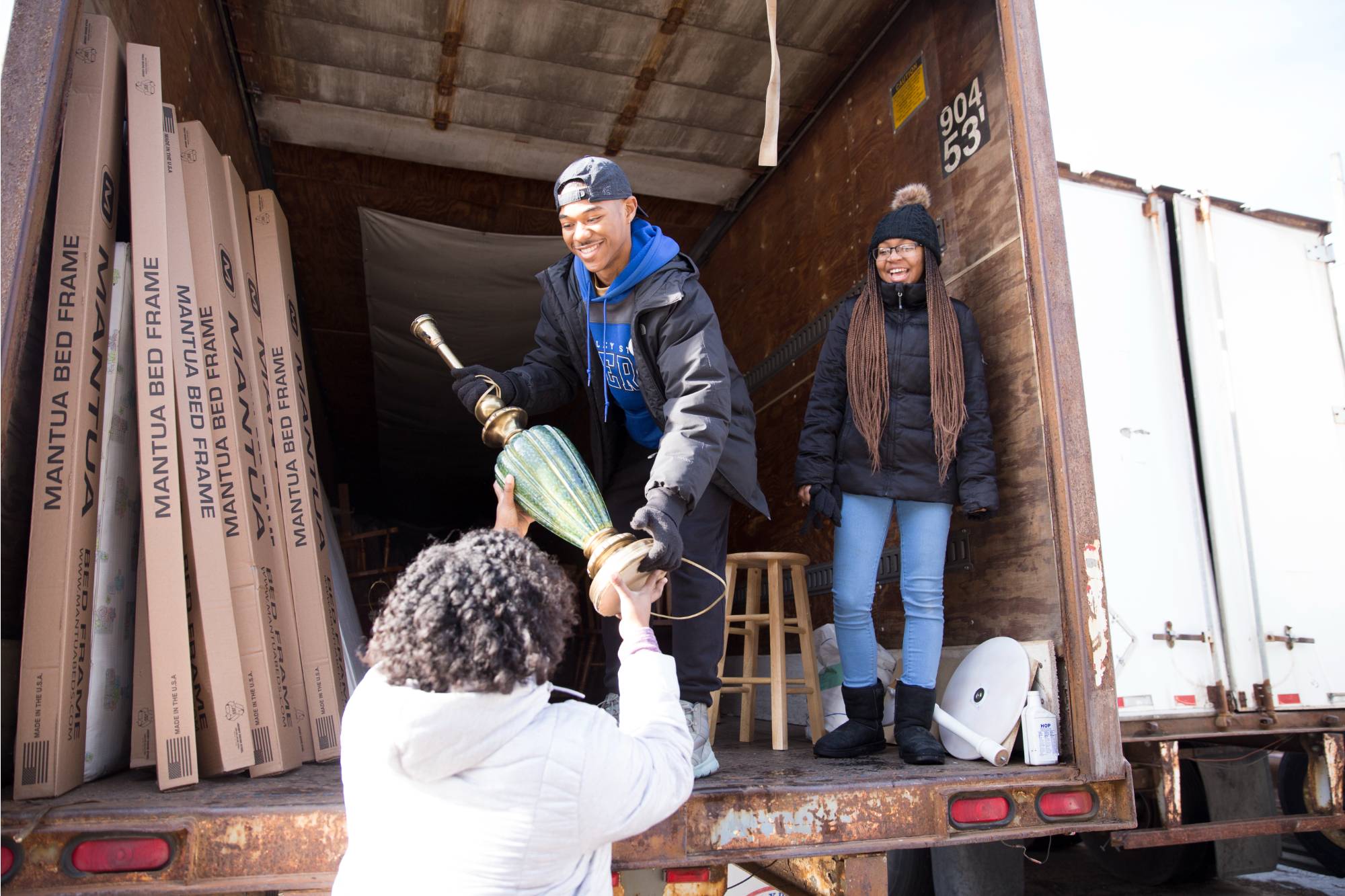 A student stands in a moving truck and passes a lamp to a woman